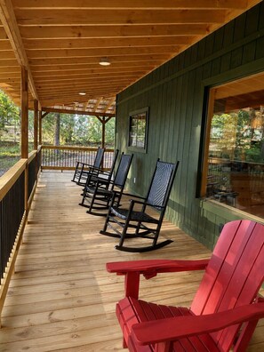 A covered porch with wooden flooring, rocking chairs, and a red Adirondack chair.