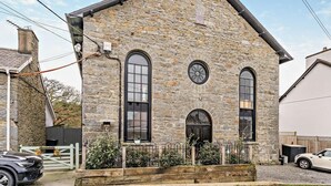 Ein Steinhaus mit Giebeldach, großen Bogenfenstern und einer kleinen Veranda mit Metallgeländer.