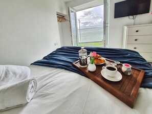 Une chambre avec un lit, un plateau contenant des articles pour le petit-déjeuner, un téléviseur fixé au mur et une vue sur la mer.