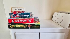 Et stabel af brætspil på en hylde med en hvid enhed til højre.