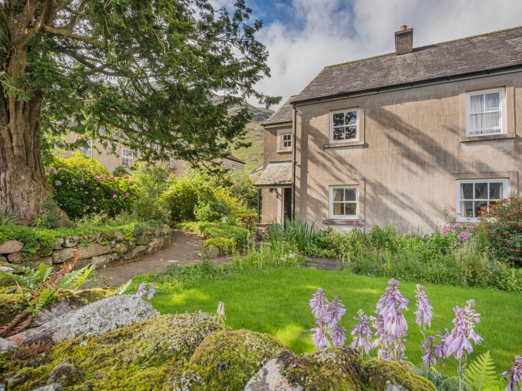 A traditional stone house with a well-maintained garden, a stone pathway, and a large tree.