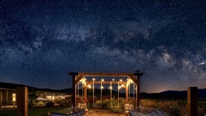 Un ciel étoilé, une pergola en bois et deux hamacs en dessous.