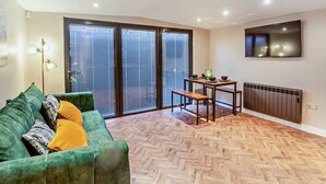 A room with a green sofa, a small wooden table with bowls, a floor lamp, and a sliding glass door leading outside. - 2 Bed in Rhyl (oc-94036) (Kinmel Bay)