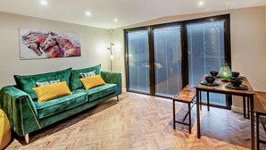 A room with a green sofa, a table with bowls, a painting on the wall, and a large window with blinds. - 2 Bed in Rhyl (oc-94036) (Kinmel Bay)