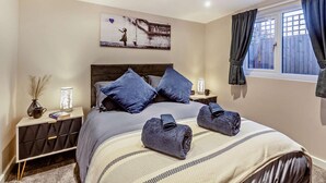 A bedroom with a bed, pillows, a bedside table with a lamp, a wall art piece, and a window with curtains. - 2 Bed in Rhyl (oc-94036) (Kinmel Bay)