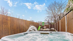 A hot tub with a waterfall feature, surrounded by a wooden fence and a patio area with outdoor furniture. - 2 Bed in Rhyl (oc-94036) (Kinmel Bay)