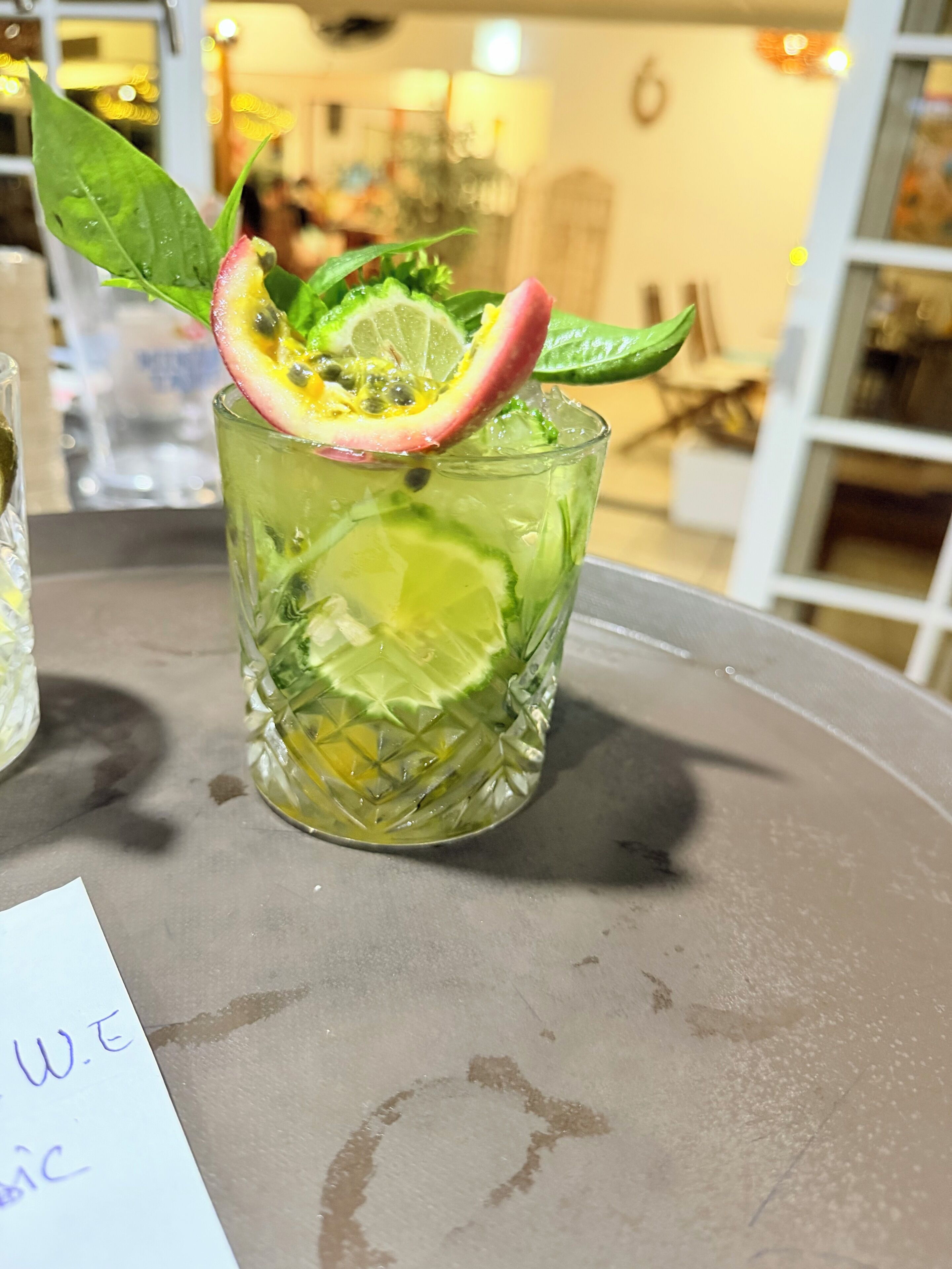 Un vaso con rodaja de lima, hojas de menta y una guarnición rosada sobre una mesa.