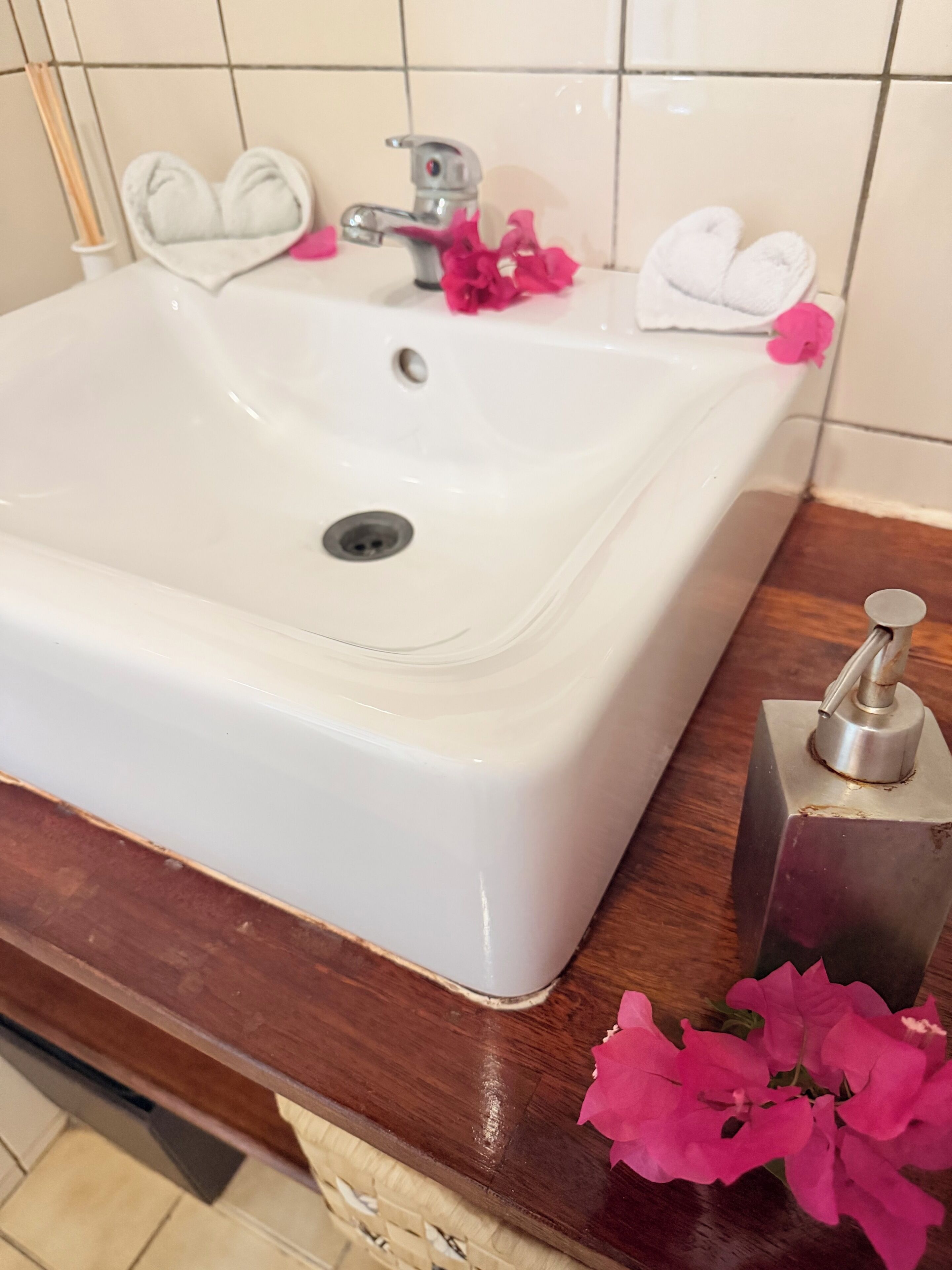 A white bathroom sink with a chrome faucet, a white towel holder, and pink flowers on the counter.