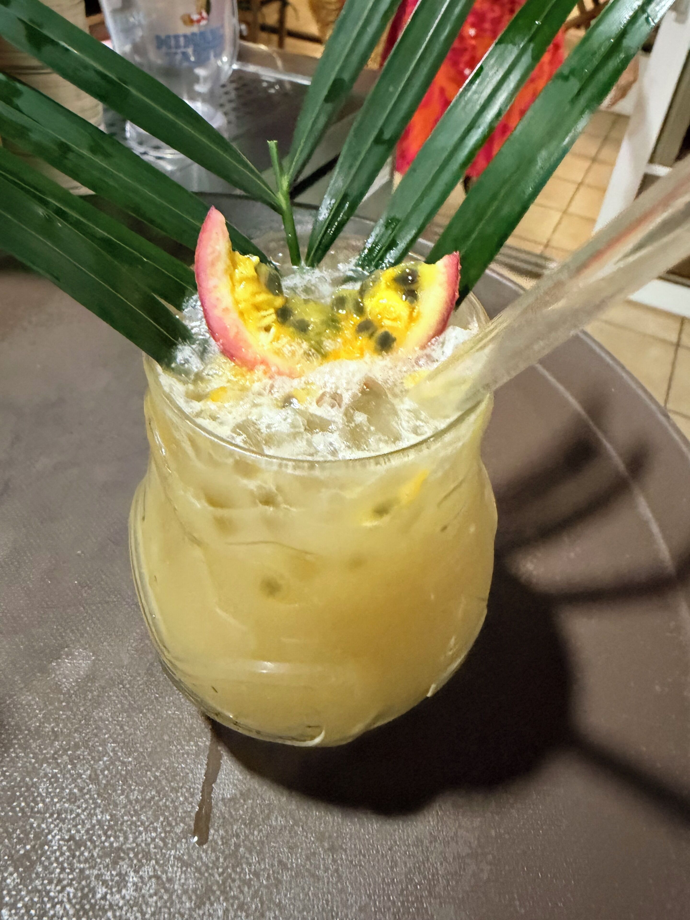 Un verre contenant une boisson jaune, une tranche de fruit et des feuilles vertes sur une table.