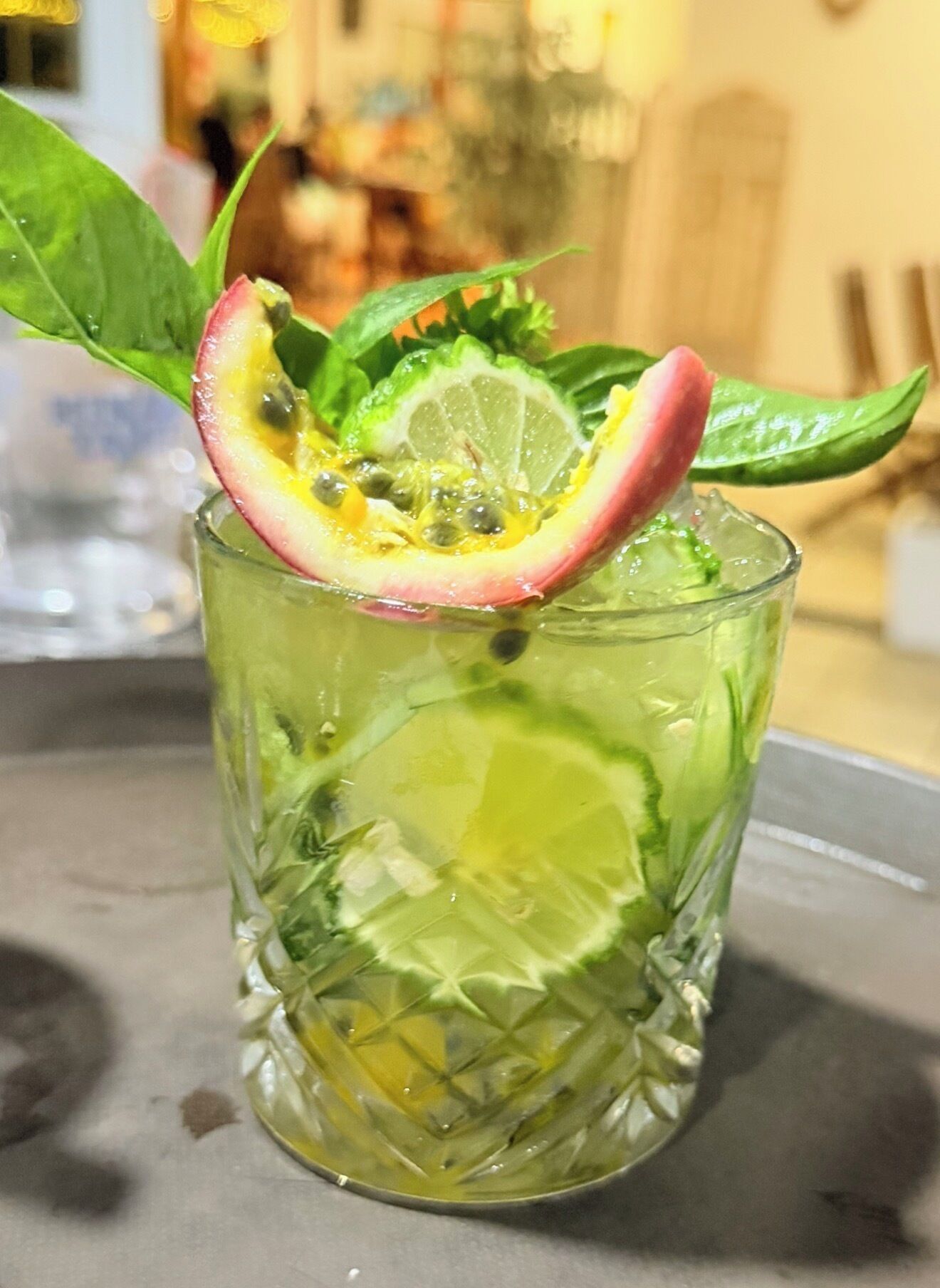 Un verre contenant une boisson agrémentée d’un quartier de citron vert, de menthe et d’une tranche de fruit, peut-être un kiwi ou un fruit de la passion.
