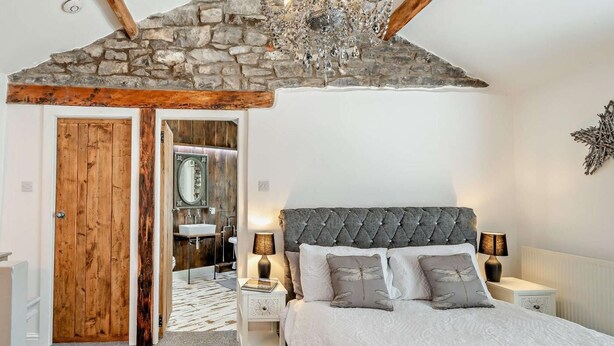 Un dormitorio con techo de piedra, puerta de madera y cama con ropa de cama gris y almohadas decorativas.