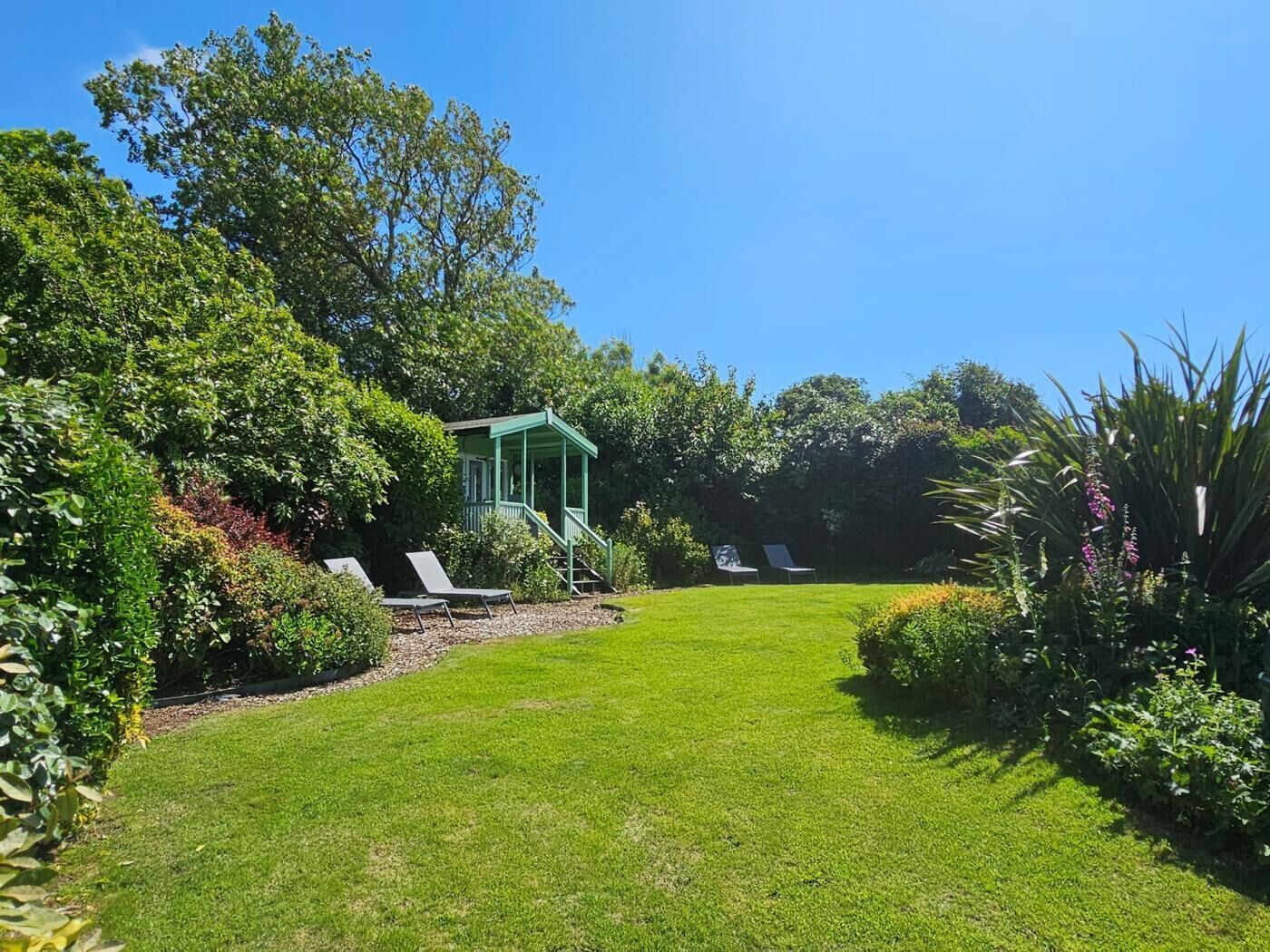 A well-maintained garden with a gazebo, two lounge chairs, and a variety of plants.