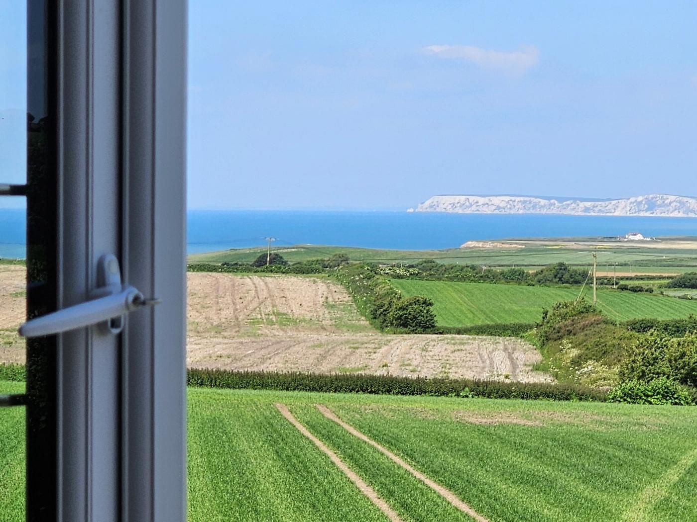 Uitzicht door een raam op een landschap met groene velden, een onverhard pad en een verre kustlijn met kliffen.