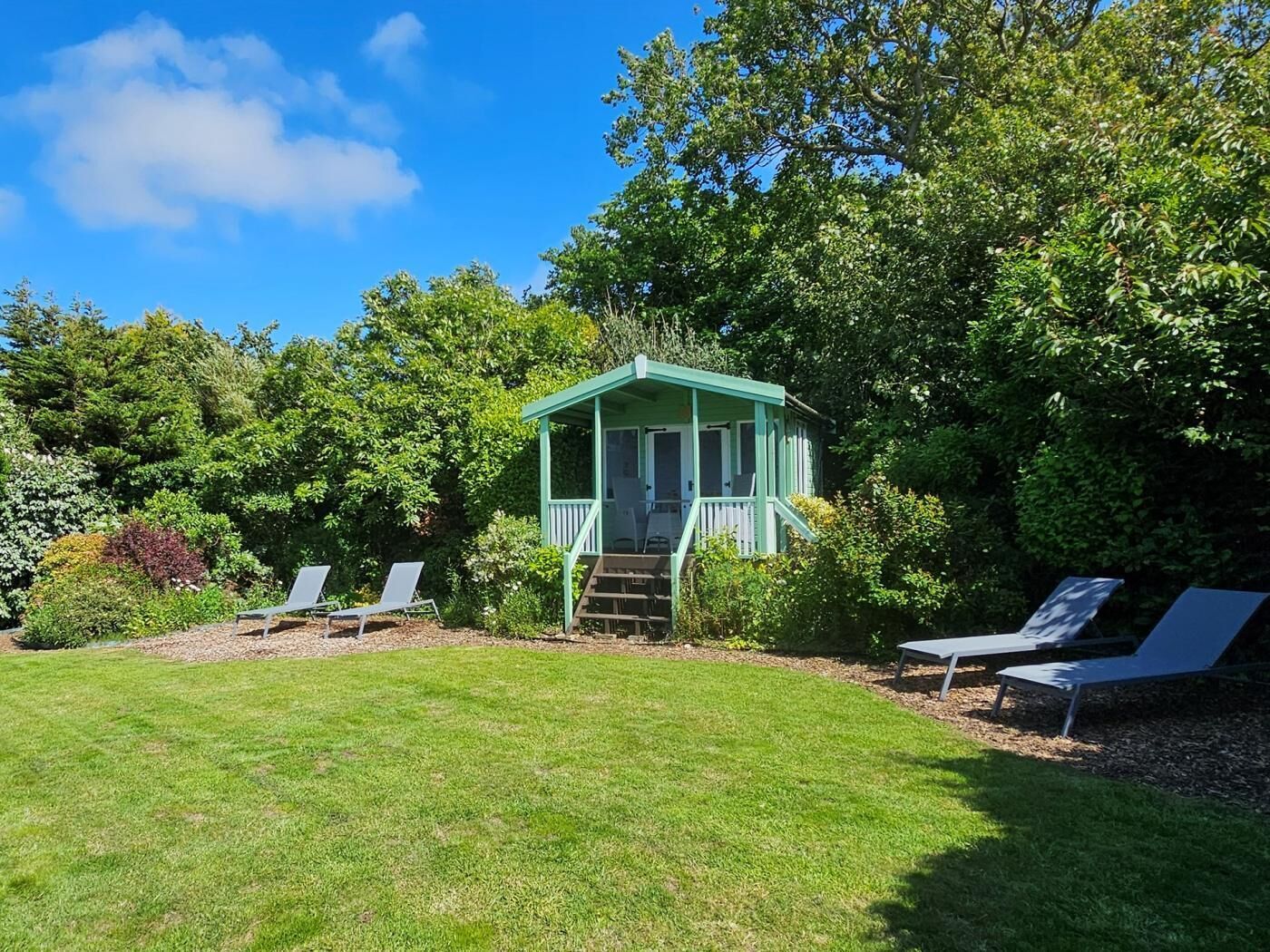 A small gazebo with a porch, surrounded by a well-maintained lawn and various shrubs.