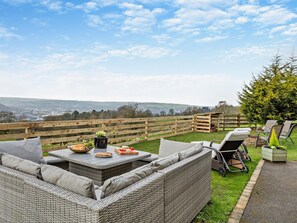 An outdoor seating area with wicker furniture, a table with food, and a view of the countryside. - 3 Bed in Keighley (oc-94182) (West Morton)