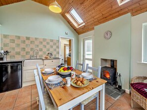 A cozy kitchen with a dining table set for breakfast, a fireplace, and a clock on the wall. - 1 Bed in Keswick (oc-94245) (Keswick)