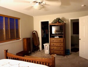 Ein Schlafzimmer mit Bett, Holzkommode, TV-Standfuß, Kleiderschrank und Deckenventilator.