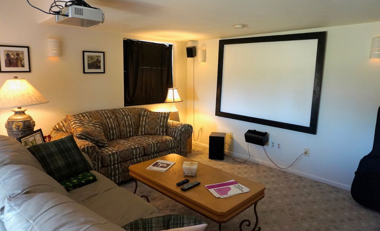 Una sala de estar con sofá, mesa de centro, pantalla de proyector y televisión.