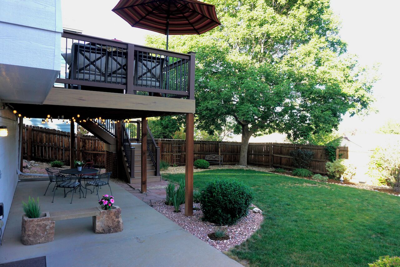A backyard patio with a table and chairs, a wooden deck, and a covered seating area.