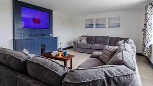 Ett vardagsrum med en platt-TV, grå soffor, ett soffbord och konst på väggarna.