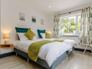 A double bed with white and green bedding, a bedside table with a lamp, and a window with curtains. - 5 Bed in Penzance (oc-82155) (Gulval)