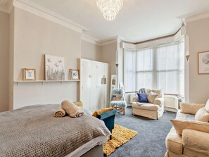 A bedroom with a large bed, a sitting area with a chair and sofa, a wardrobe, and artwork on the walls. - 2 Bed in Lytham St. Annes (oc-94212) (Saint Anne's on the Sea)