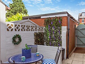 Eine Terrasse mit rundem Tisch und Stühlen, einem Blumentopf und einer Wand mit Kletterpflanzen.