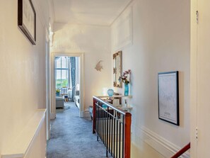 A hallway with a wooden railing, a framed map of London, and a door leading to a room with a bed and a window. - 2 Bed in Lytham St. Annes (oc-94212) (Saint Anne's on the Sea)