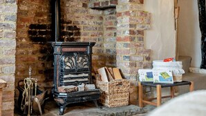 A rustic room with a brick fireplace, a vintage stove, a wicker basket, and a small table with boxes. - 2 Bed in Hastings (oc-94200) (Pett)