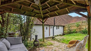 A covered patio with a sofa, a wicker chair, and a table with croissants. - 2 Bed in Hastings (oc-94200) (Pett)