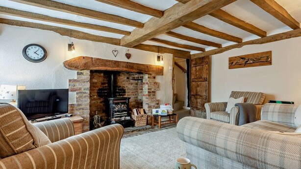 A cozy living room with a fireplace, wooden beams, a clock, and a television. - 2 Bed in Hastings (oc-94200) (Pett)