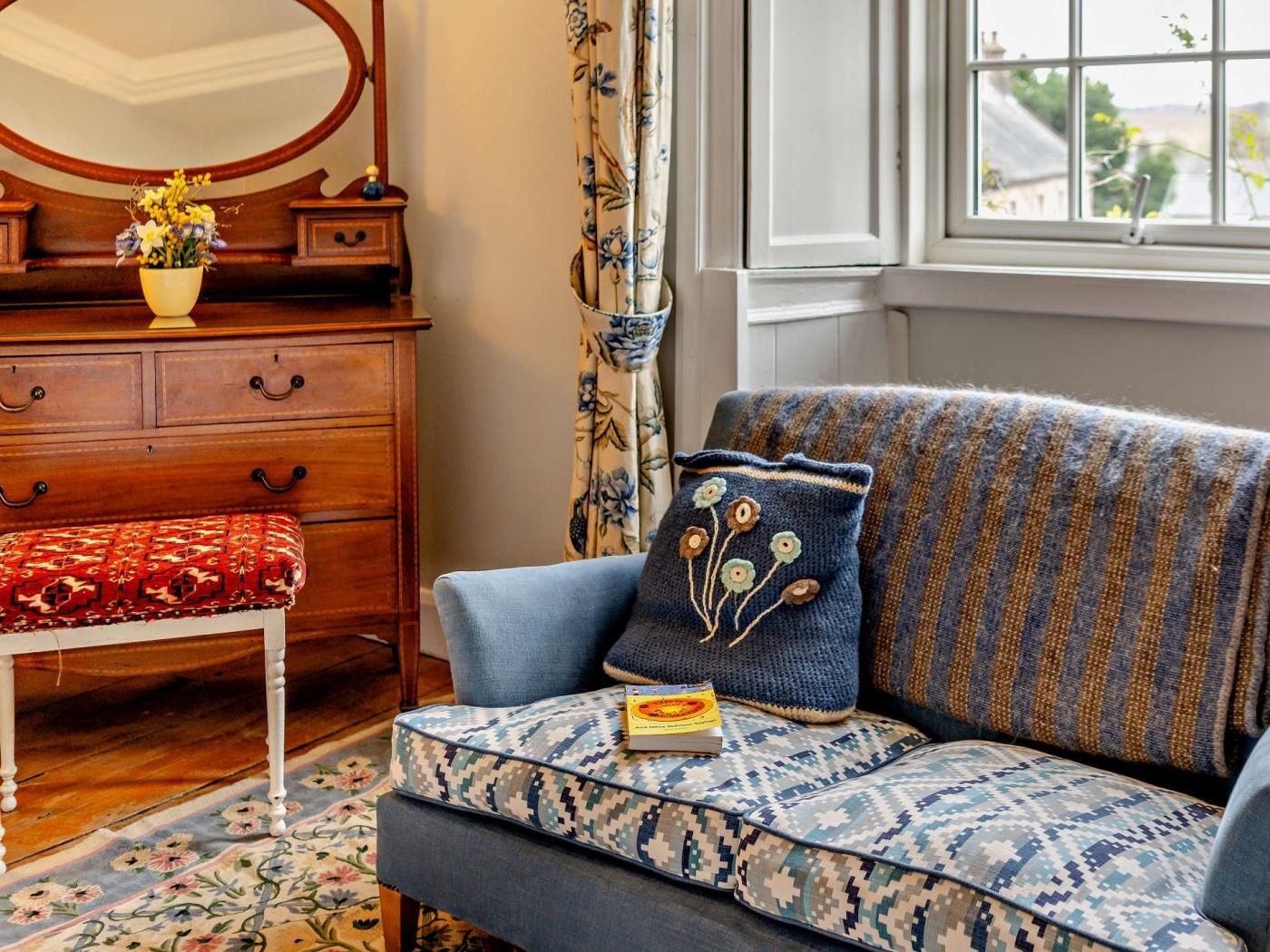 A cozy living room with a patterned sofa, a wooden side table, and a floral rug.