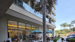 Un bâtiment moderne doté d’une façade en verre, d’une terrasse avec des parasols et d’un jardin bien entretenu.