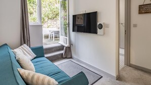 Un salon moderne avec un canapé de couleur turquoise, un téléviseur à écran plat et une vue sur un jardin, visible à travers une porte vitrée.