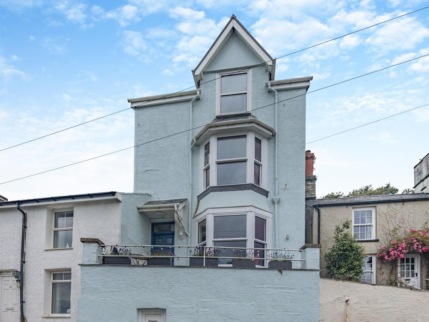Un bâtiment à deux étages, doté d’une baie vitrée au deuxième étage, d’une porte bien visible et d’un petit balcon avec des balustrades.