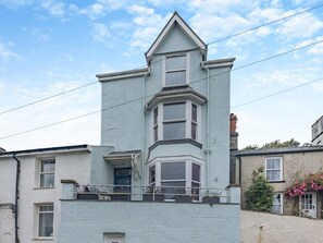 A two-story building with a bay window on the second floor, a visible door, and a small balcony with railings. - 4 Bed in Aberdovey (oc-94232) (Aberdovey)