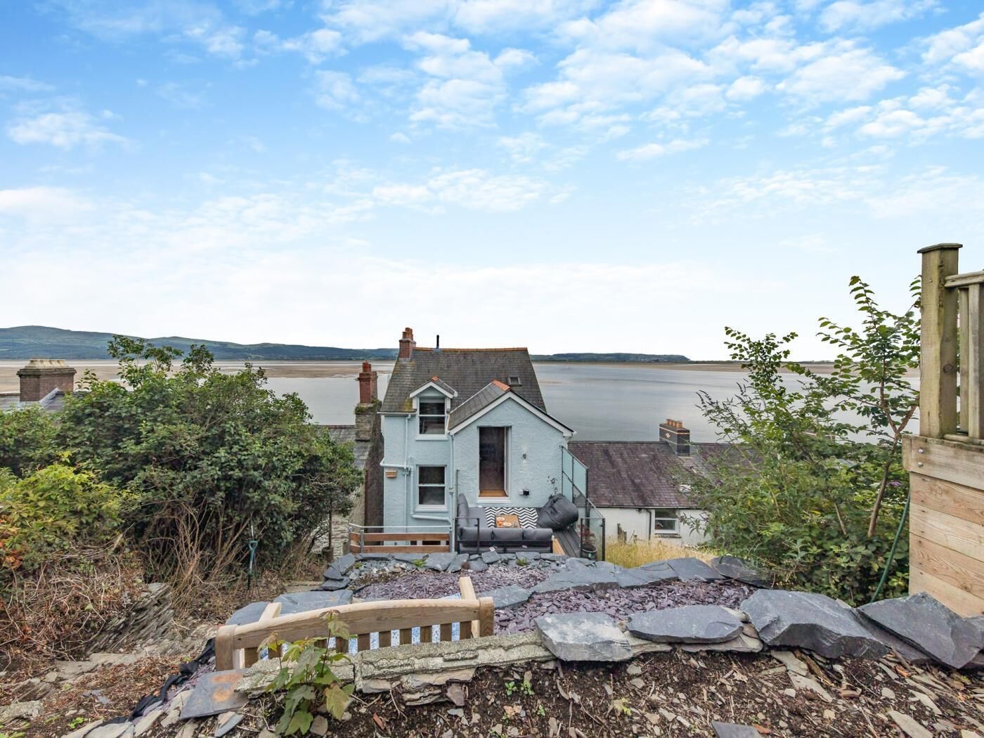 A coastal house with a stone pathway leading to the entrance, overlooking a body of water.