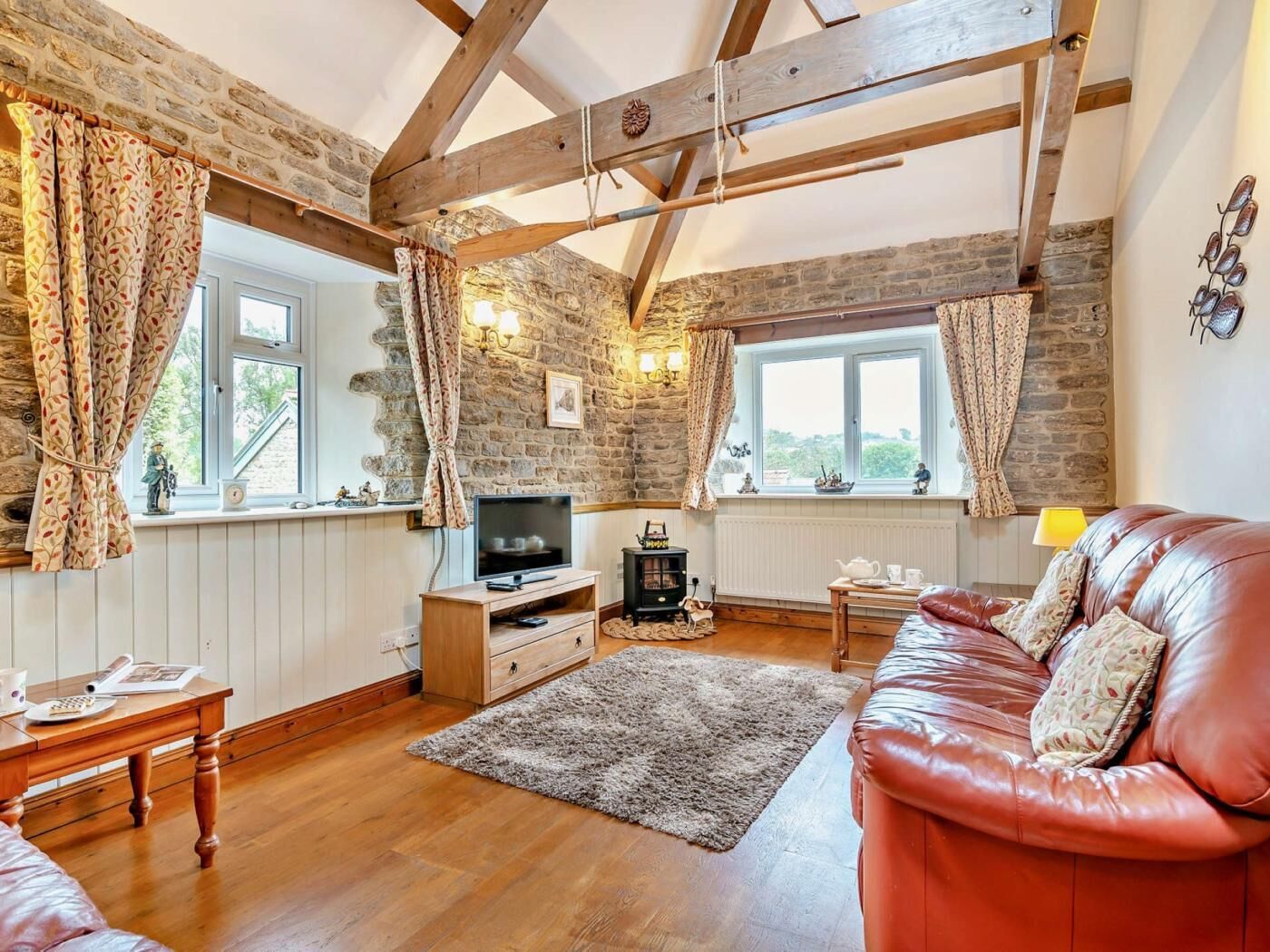 A cozy living room with a stone wall, wooden beams, a leather sofa, a TV, and a fireplace.