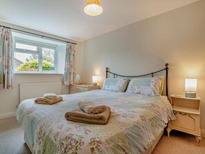 Une chambre à coucher avec un lit, deux tables de chevet, une fenêtre avec des rideaux et un radiateur.