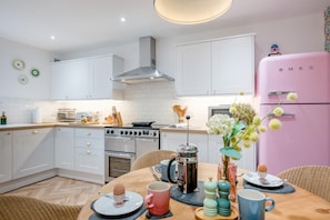Eine moderne Küche mit weißen Schränken, einem pinken Kühlschrank und einem Essbereich mit einem für das Frühstück gedecktem Holztisch.