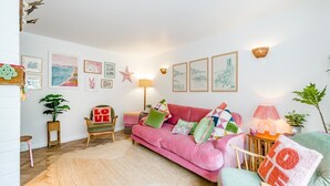 Una sala de estar acogedora con un sofá rosa, un sillón verde y una mesa de centro de madera. Hay cuadros en la pared y un adorno con forma de estrella.