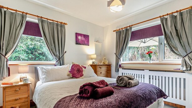 A bedroom with a bed, bedside table, lamp, and windows with curtains. - 1 Bed in Redruth (oc-90897) (Redruth)