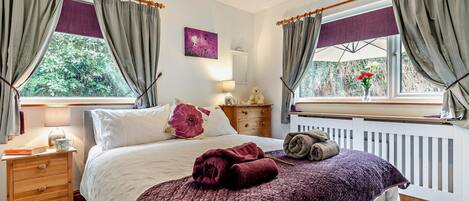 A bedroom with a bed, bedside table, lamp, and windows with curtains.