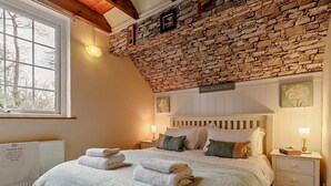 Ein Schlafzimmer mit Steinwand, einem Bett mit weißer Bettwäsche, zwei Nachttischen und einem Fenster.