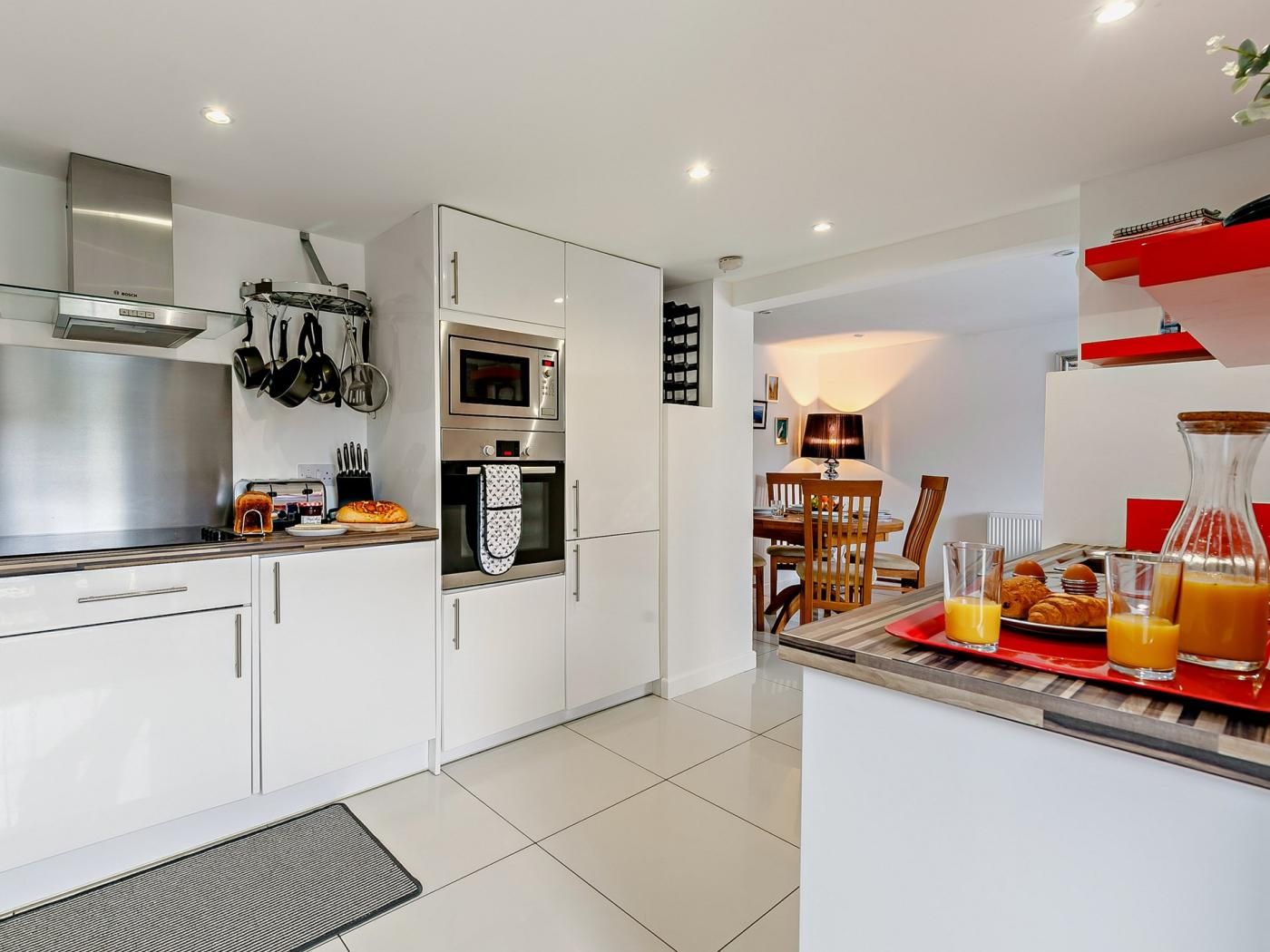 A modern kitchen with white cabinets, a built-in oven, and a dining area with a table and chairs.