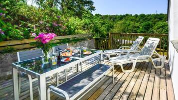 A deck with a table and chairs, surrounded by greenery.