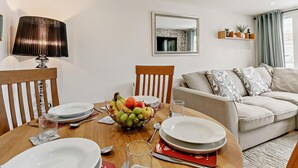 Ein Essbereich mit Tisch für vier Personen, einer Obstschale und einer Couch im Hintergrund.