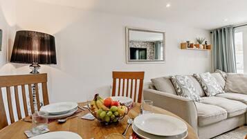 A dining area with a table set for four, a bowl of fruit, and a sofa in the background.