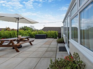 A patio with a picnic table and umbrella, surrounded by greenery and a house with large windows. - 2 Bed in Saundersfoot (oc-94207) (Saundersfoot)