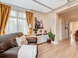 A living room with a brown leather sofa, a white throw blanket, a potted plant, and a radiator. - 2 Bed in Saundersfoot (oc-94207) (Saundersfoot)